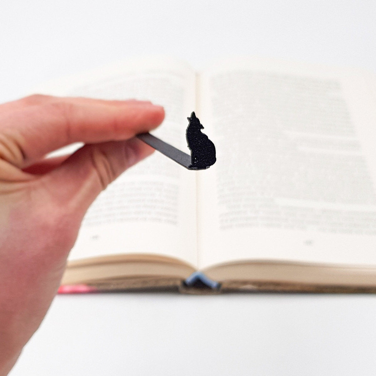 Howling Wolf metal bookmark held up beside an open book