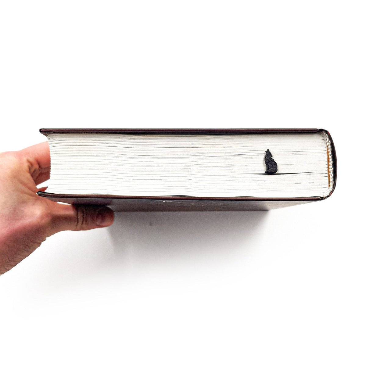 Howling Wolf metal bookmark held in a hand above an open book