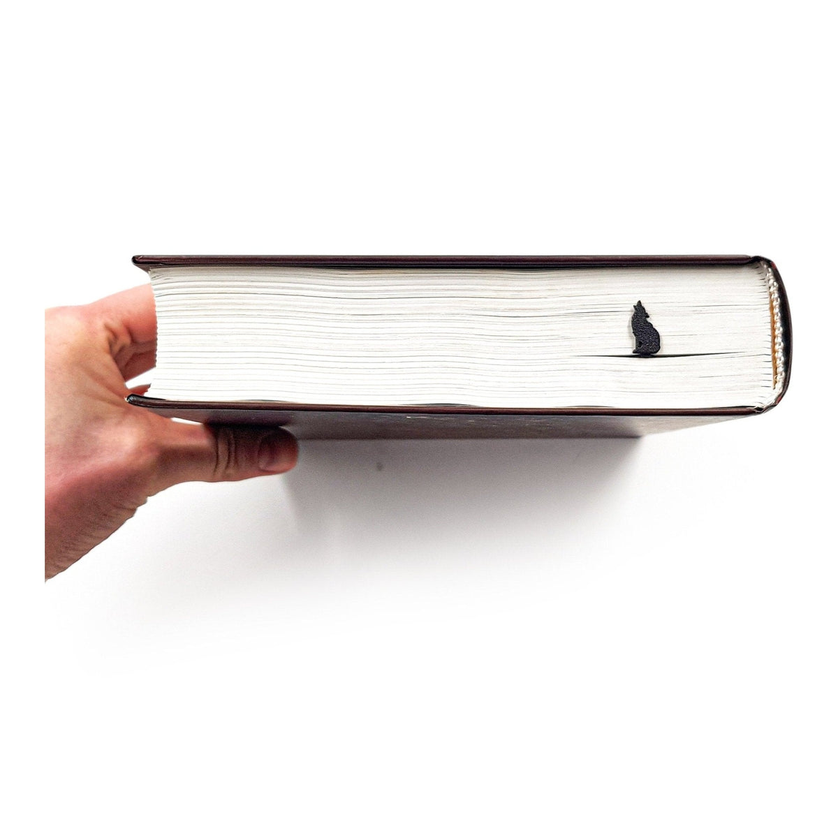 Howling Wolf metal bookmark held in a hand above an open book