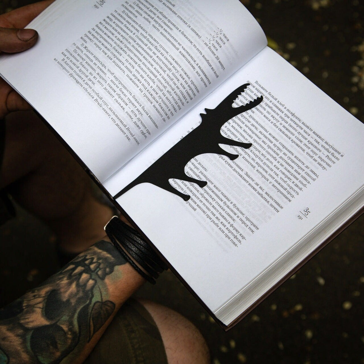 Hungry Wolf metal bookmark held in a hand above an open book