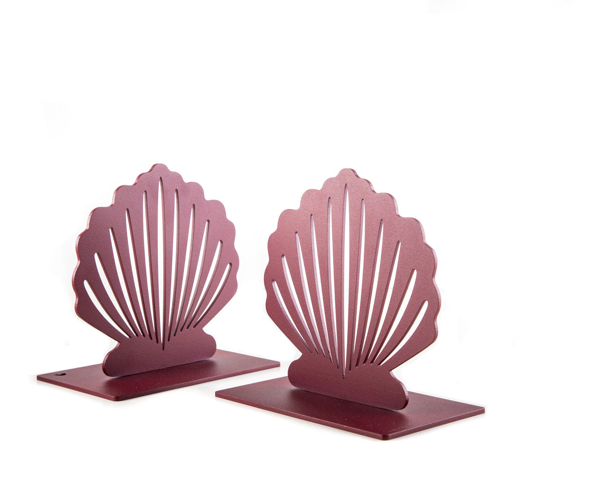 Pair of red metal bookends shaped like sea shells, standing upright on white background. Each bookend has a minimalist cutout design and a smooth matte finish.