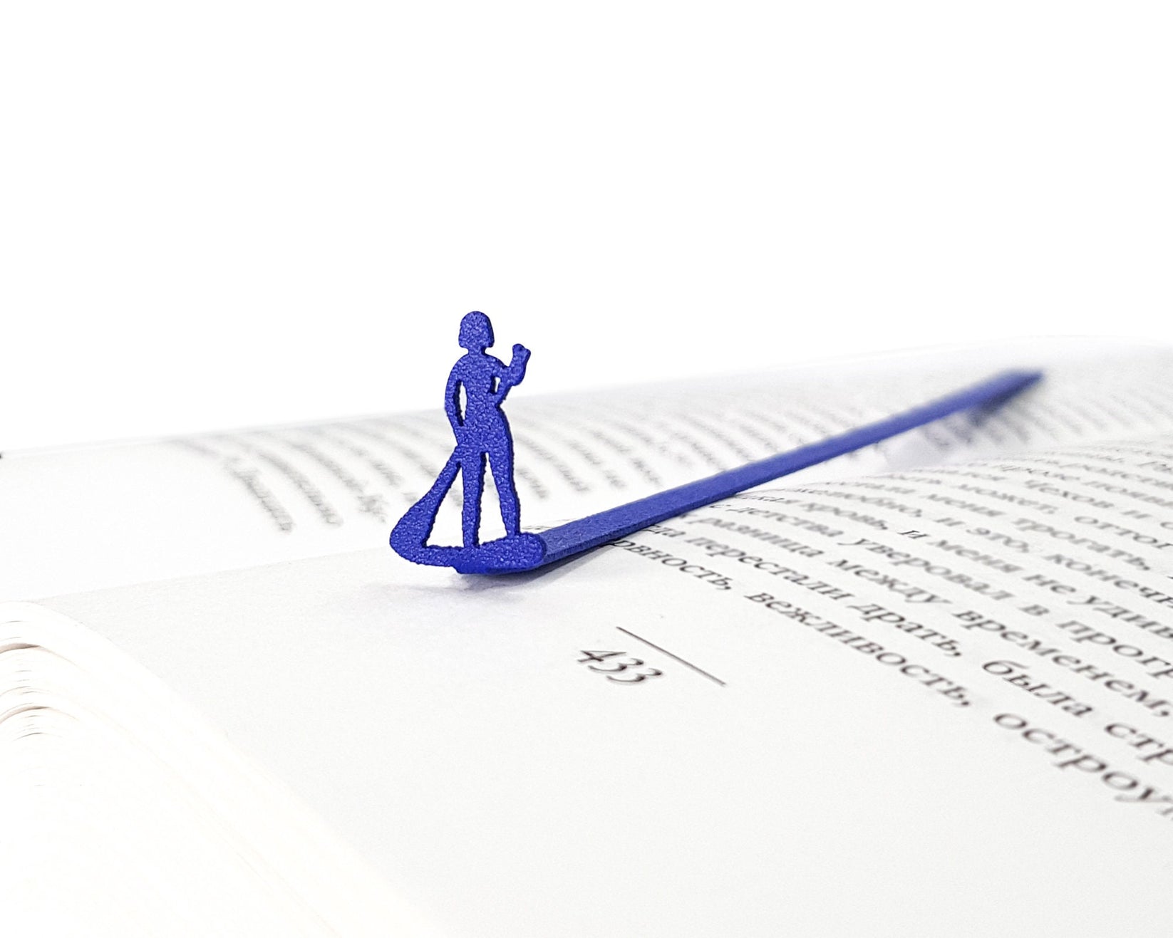 Surfer metal bookmark in blue marking a page in an open book
