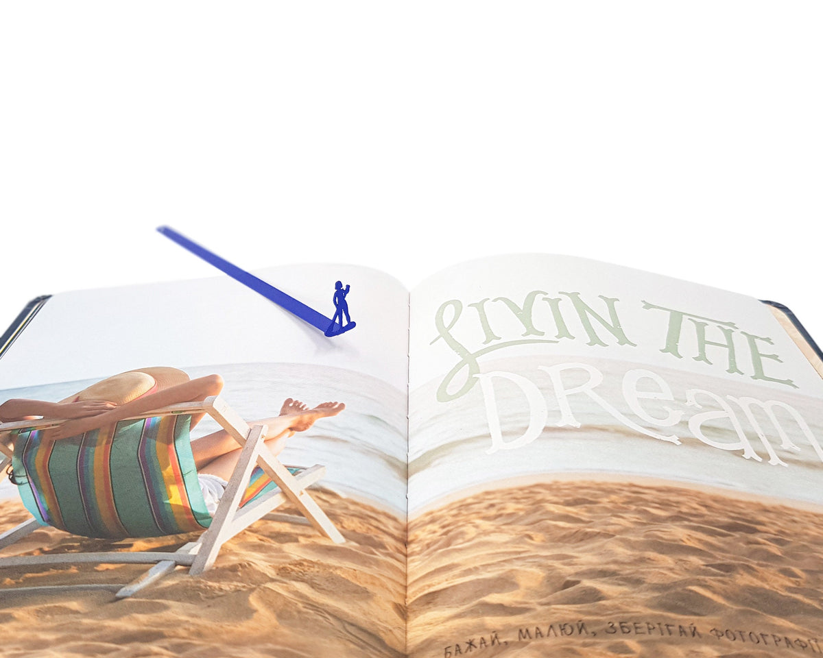Surfer metal bookmark in blue marking a page in an illustrated book
