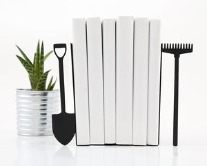 Pair of black metal bookends shaped like a garden shovel and rake, holding white books upright – perfect gift for gardeners, nature lovers, or outdoor enthusiasts. Minimalist design adds rustic charm and functional style to shelves or desks. Great for home libraries, garden rooms, or eco-inspired decor themes. Designed and made by Atelier Article on Etsy. Not mass-produced.