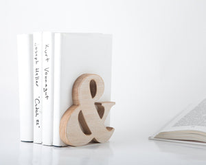 Wooden ampersand bookend supporting white hardcover books, minimalist natural wood decor for modern office or stylish home bookshelf.