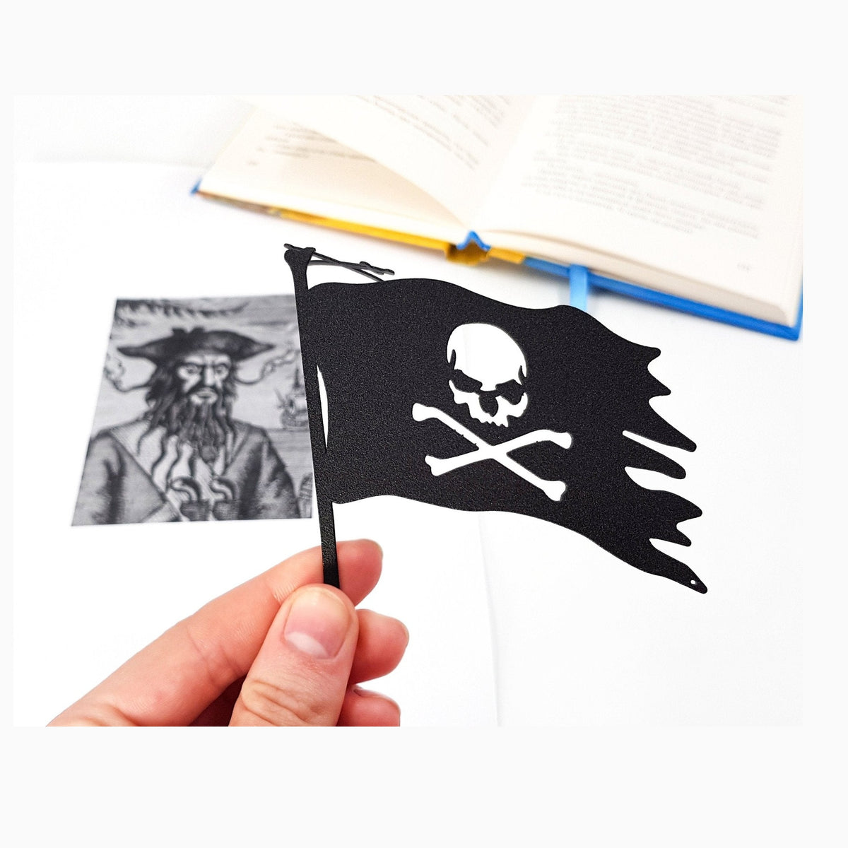 Jolly Rogers metal bookmark held in a hand above an open book