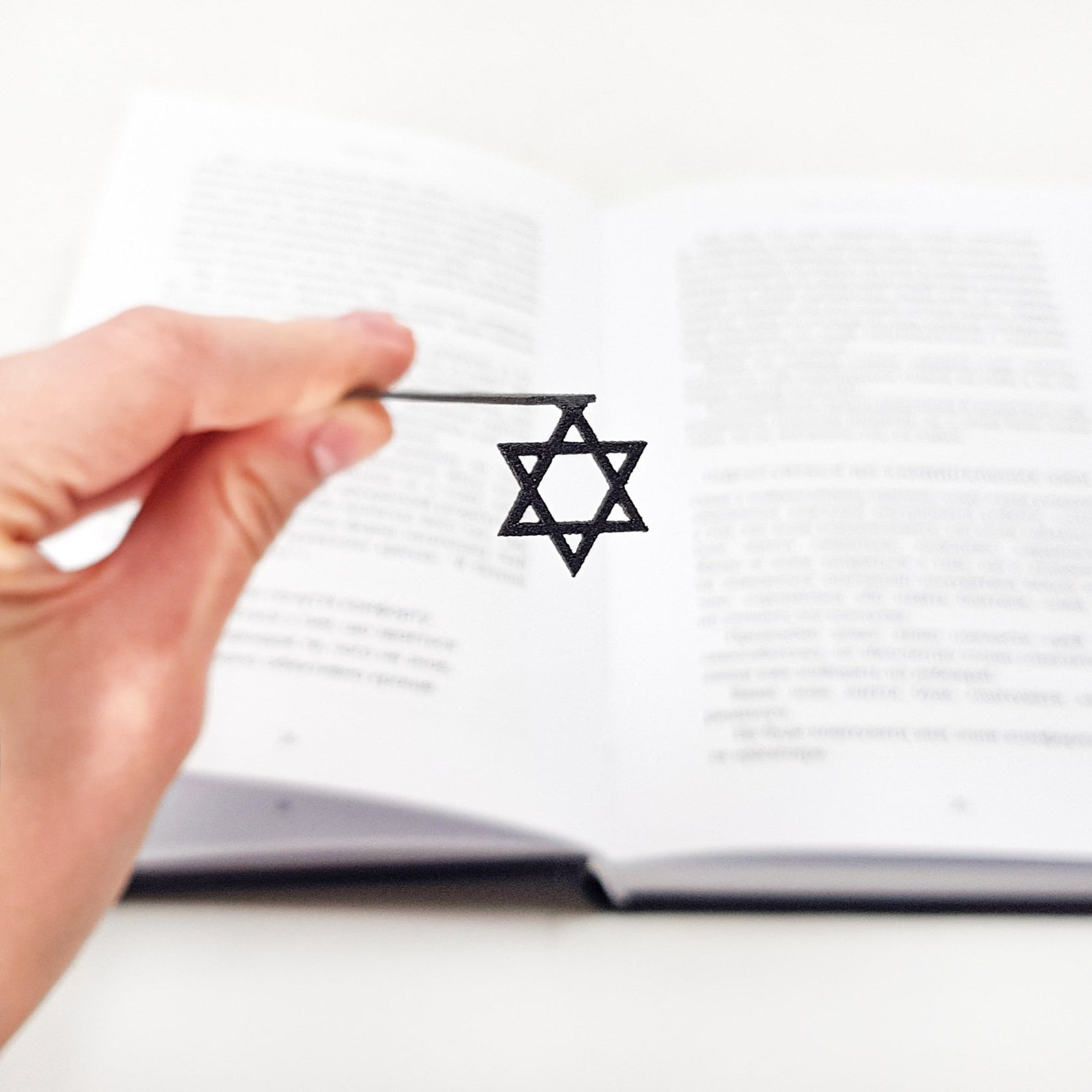 Judaical Star of David metal bookmark held in a hand above an open book