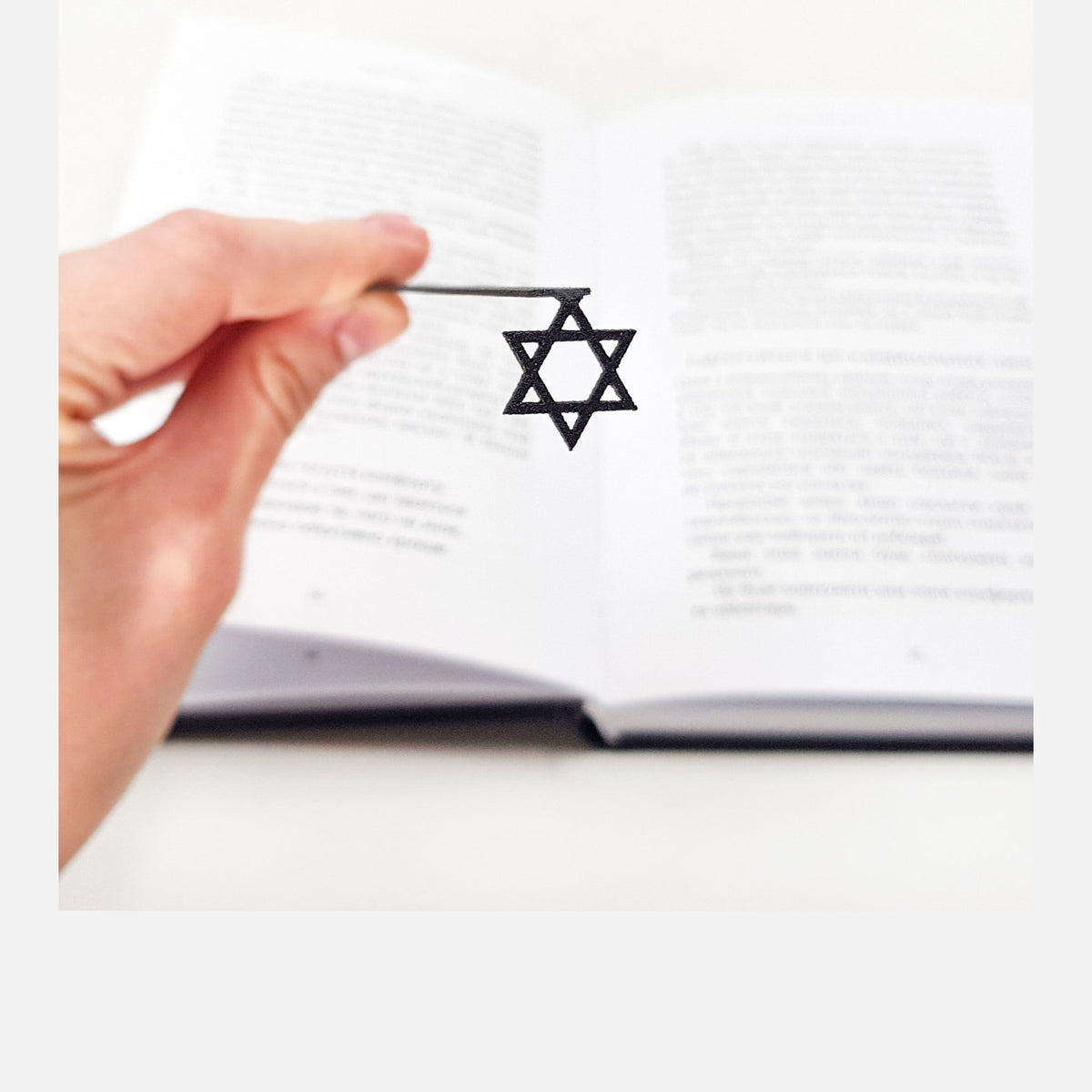 Judaical Star of David metal bookmark held in a hand above an open book