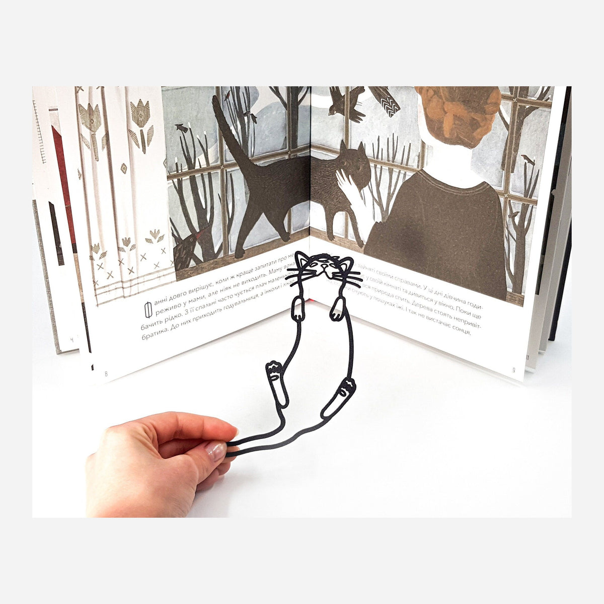 Kitty's Dream metal bookmark held in a hand above an open book