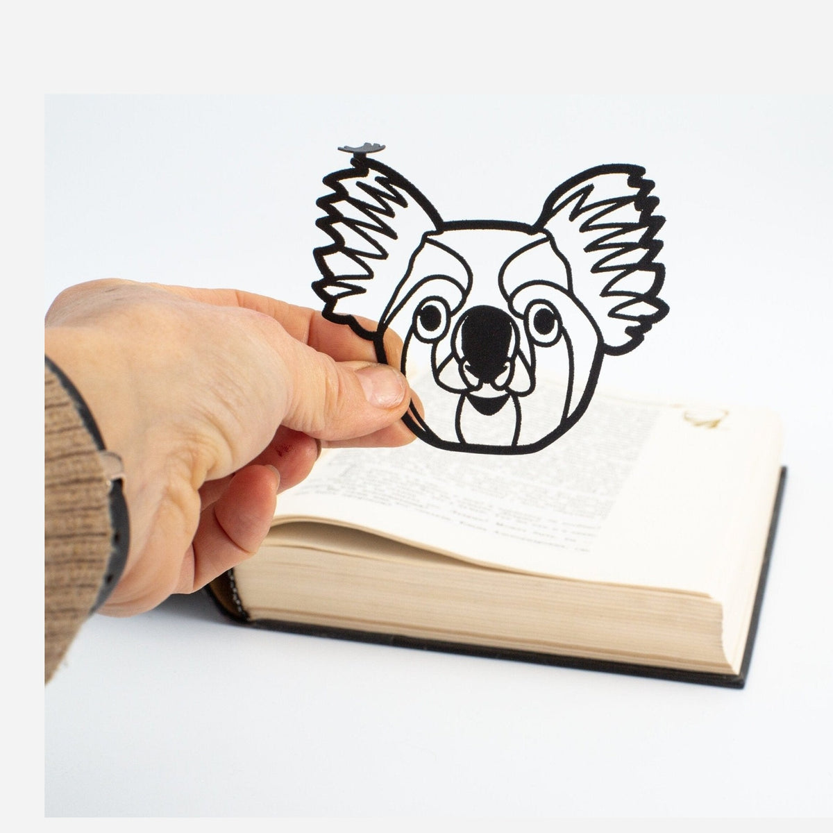 Koala metal bookmark held in a hand above an open book