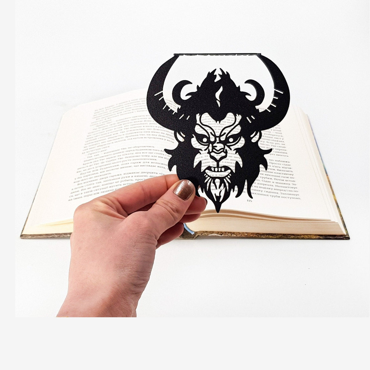 Krampus metal bookmark held in a hand above an open book