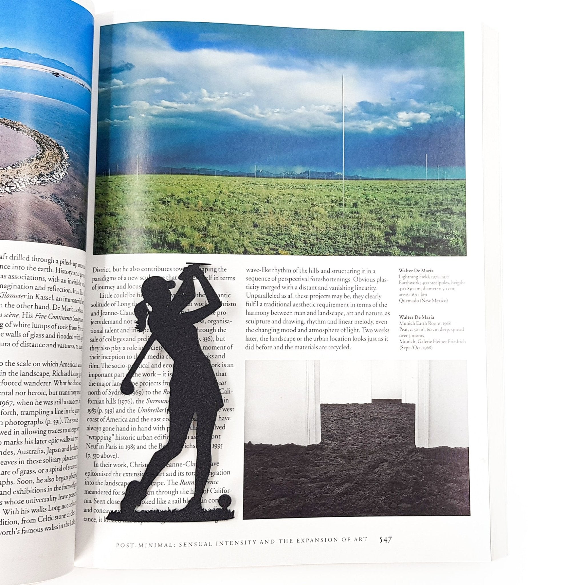 Black metal lady golf player bookmark placed on an open art book page, contrasting with the landscape photography beneath