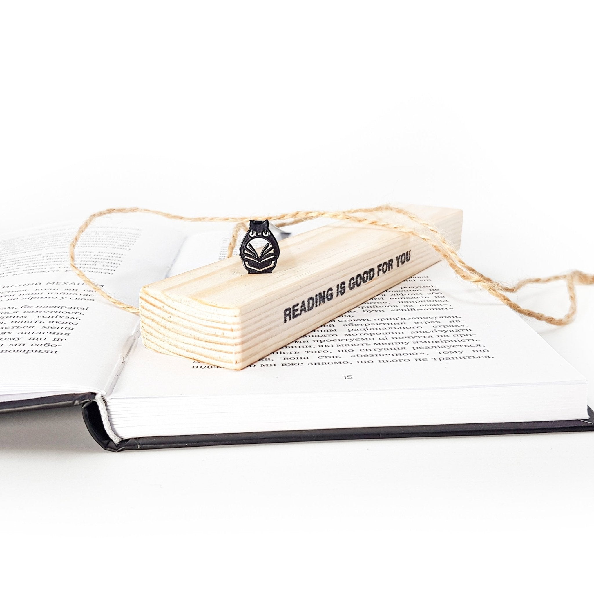 Black metal owl bookmark resting on a wooden gift block engraved with “Reading is good for you,” placed on an open book with twine wrapping for eco-friendly packaging presentation.
