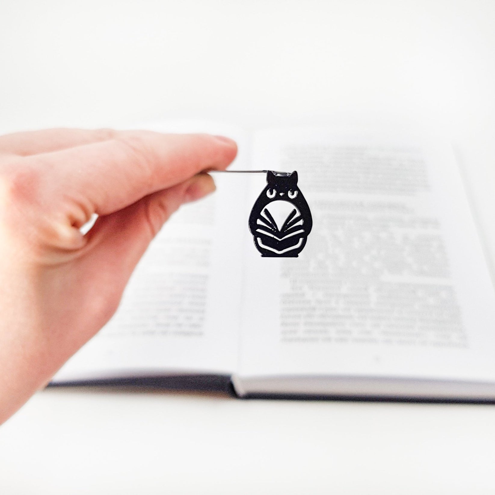 Laser Cut Metal Owl bookmark held up beside an open book