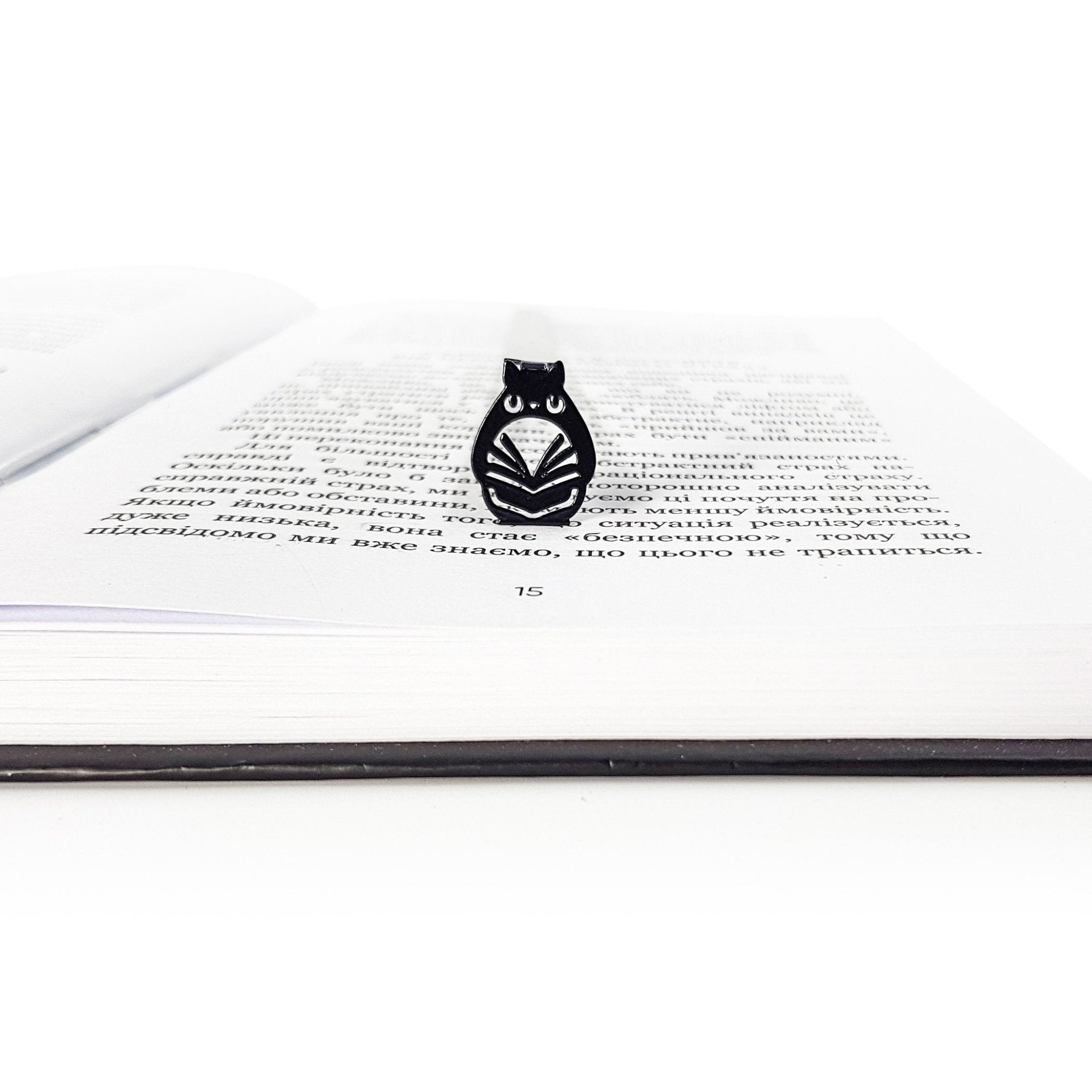 Front view of black owl metal bookmark resting inside an open book, highlighting the detailed laser cut owl shape and glossy powder coated finish.