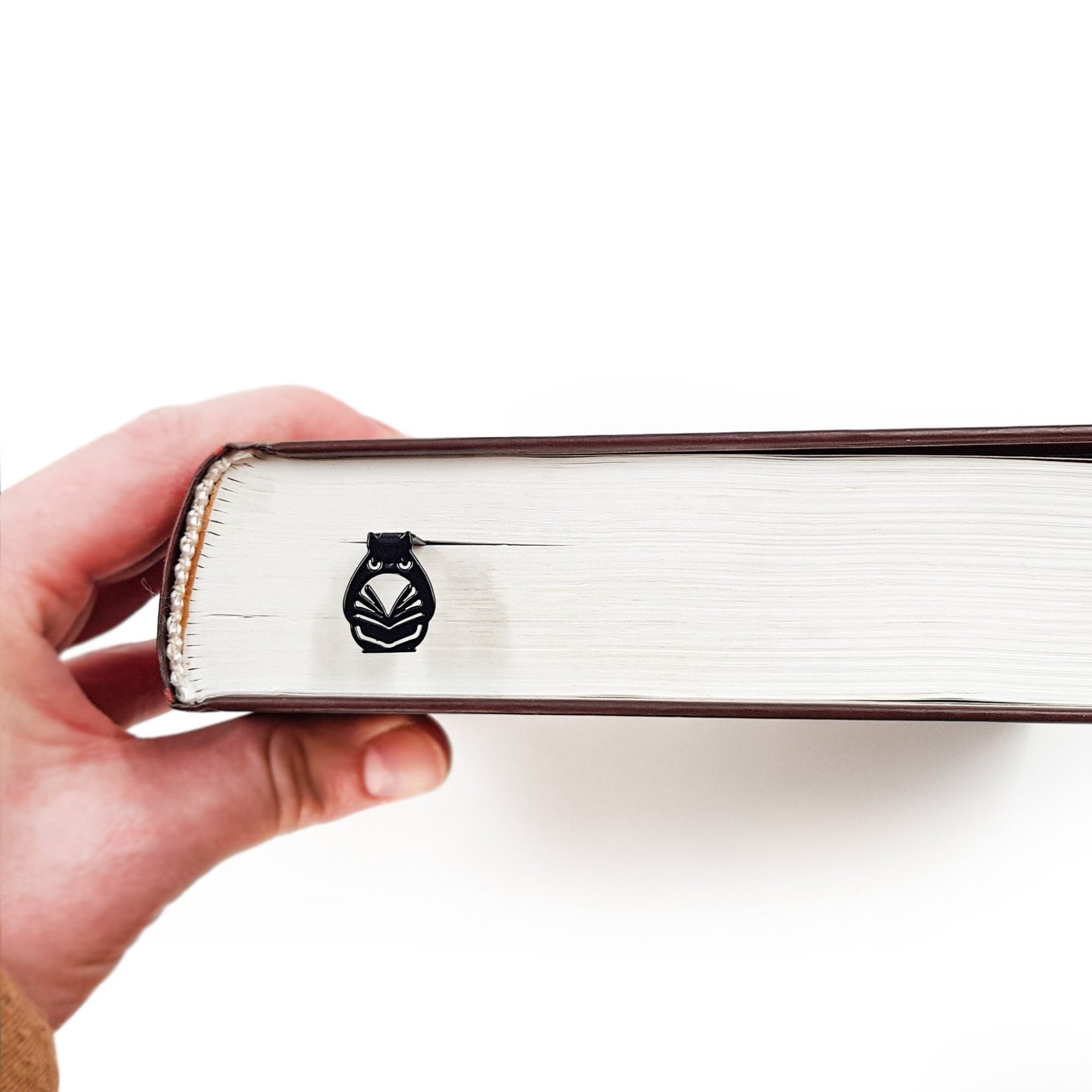 Laser Cut Metal Owl bookmark held in a hand above an open book