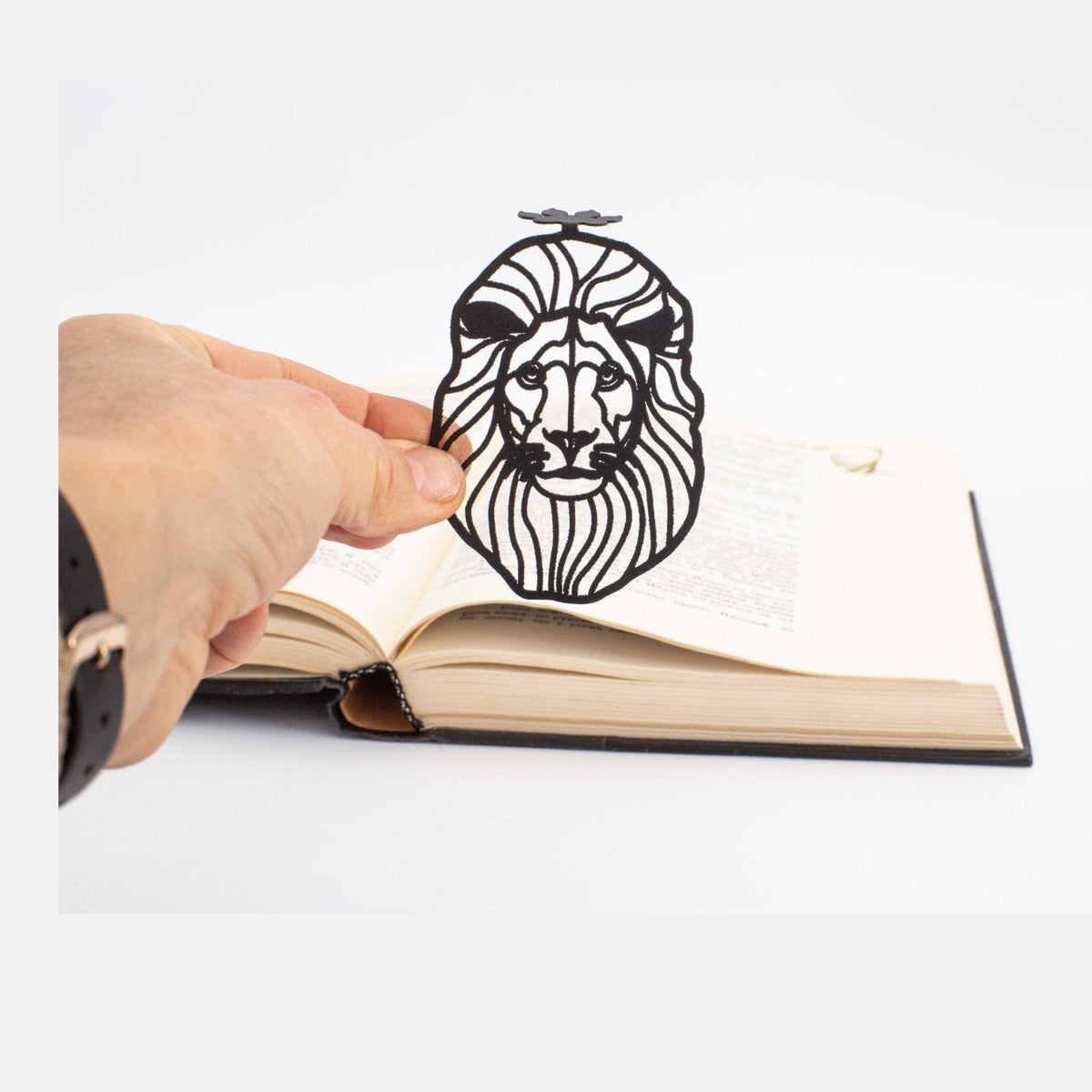 Lion Head metal bookmark held in a hand above an open book