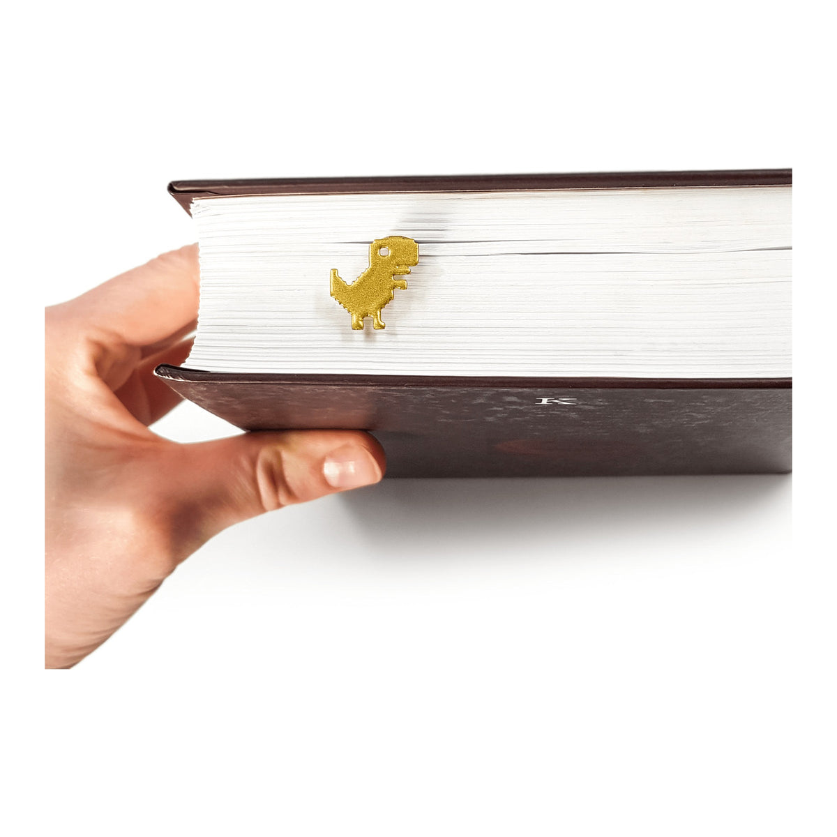 Little Dino metal bookmark in gold held in a hand above an open book