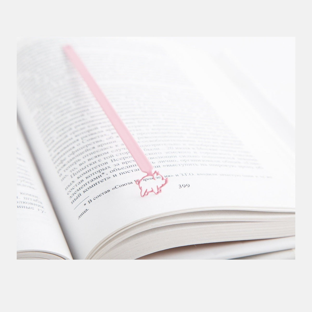 Little Piggy metal bookmark in red resting on the pages of an open book