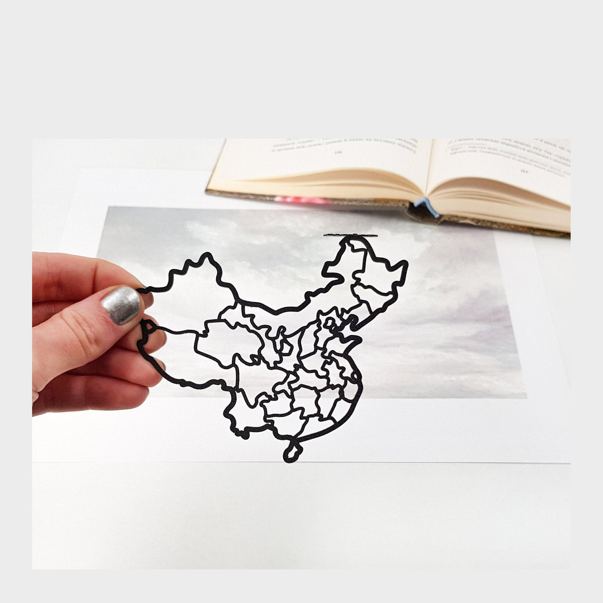 Map of China metal bookmark held in a hand above an open book