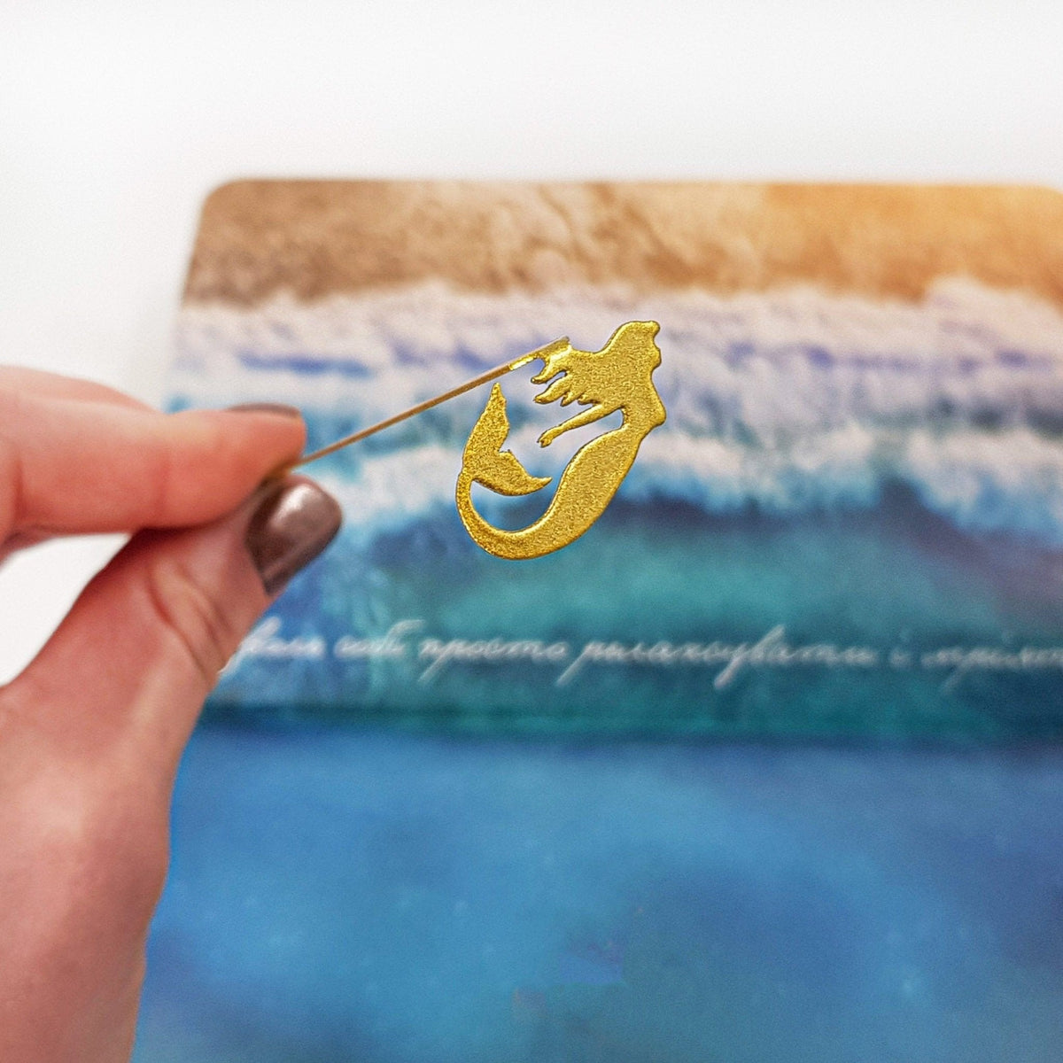 Mermaid metal bookmark in gold marking a page in an illustrated book