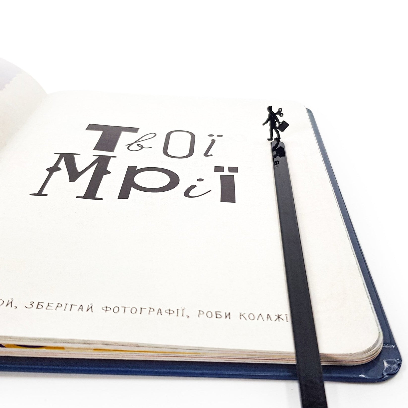 Black metal bookmark with a businesswoman silhouette standing at the top, placed inside an open notebook with minimalist typography.