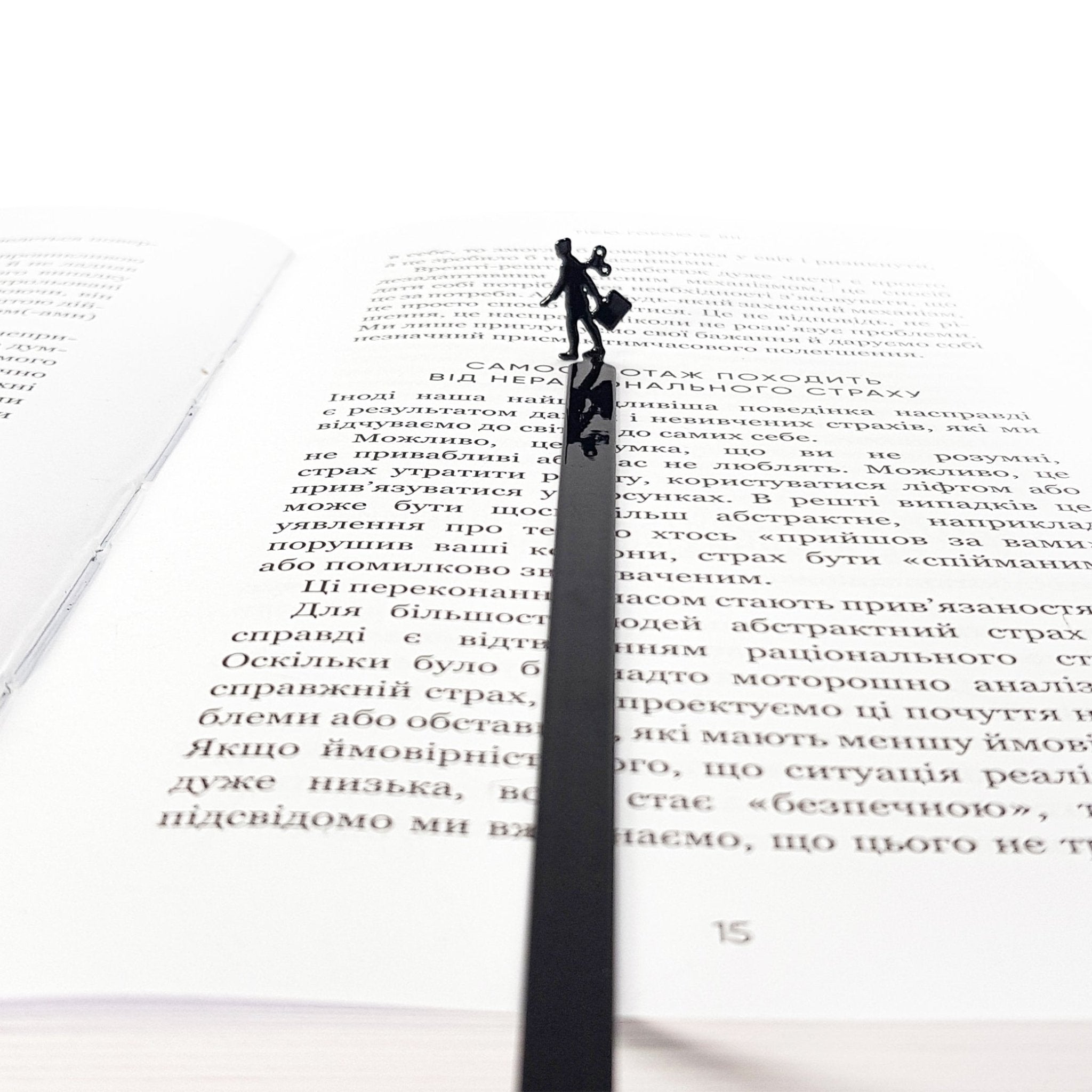 Black metal bookmark with a walking businesswoman silhouette placed inside an open book, minimalist reading accessory for modern readers.