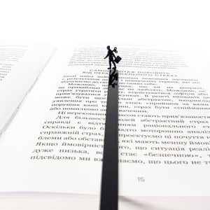 Black metal bookmark with a walking businesswoman silhouette placed inside an open book, minimalist reading accessory for modern readers.
