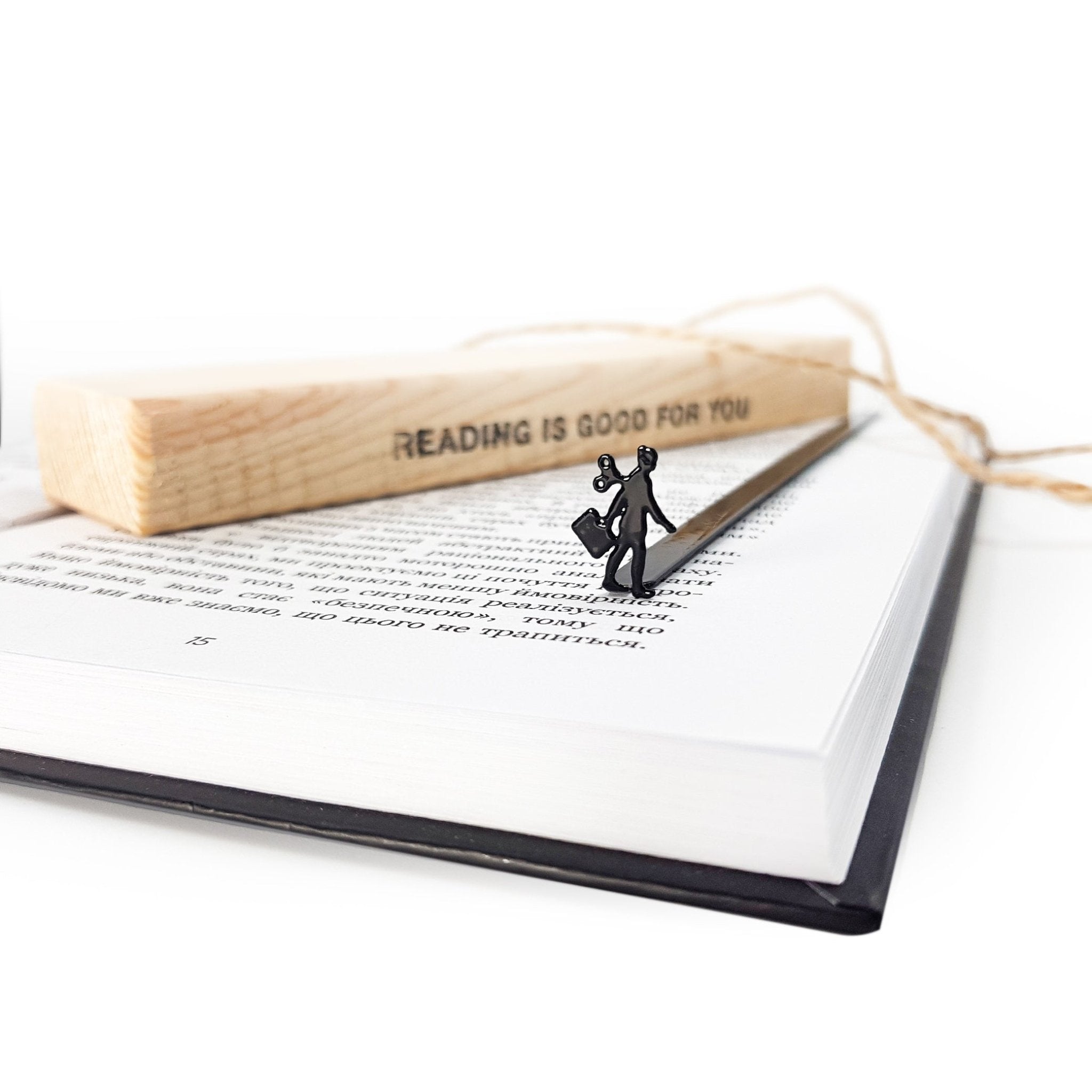 Black metal bookmark shaped like a walking businesswoman with a wind-up key, resting on an open book beside a wooden packaging block.