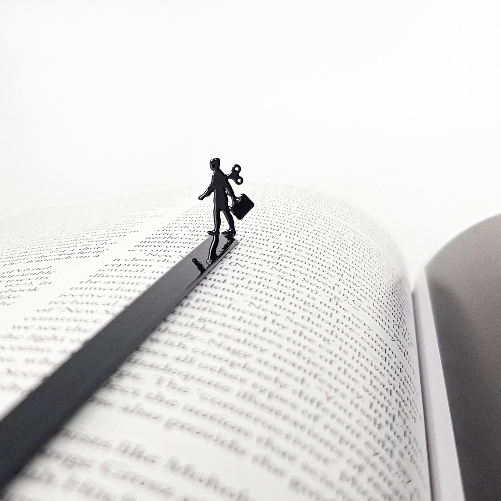 Black metal bookmark featuring a business woman silhouette with a wind up key resting on an open book page