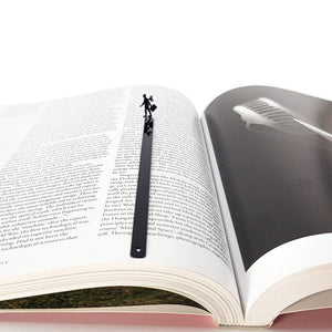 Black metal bookmark with a walking businesswoman silhouette centered in an open book, minimalist handmade reading accessory.