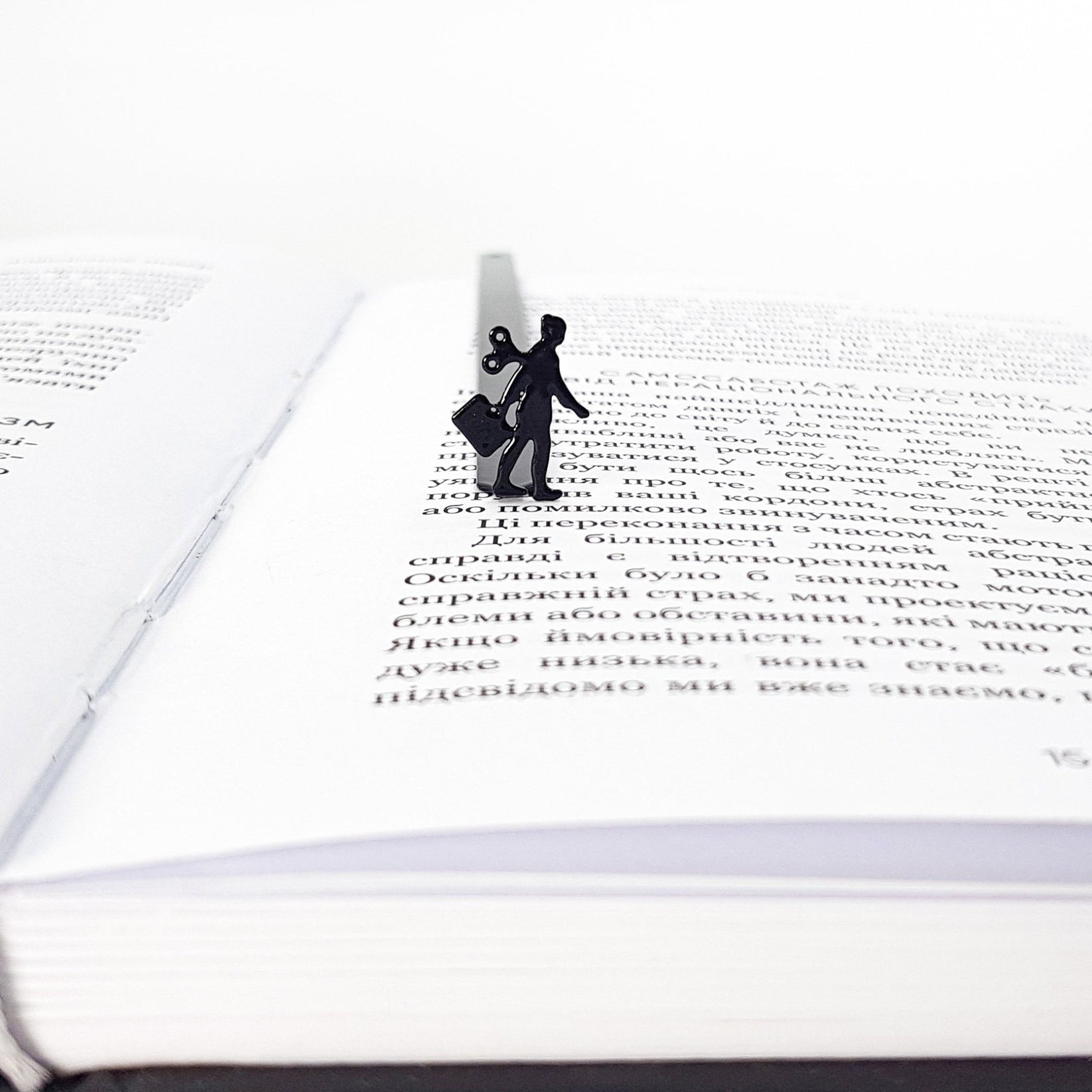 Black metal bookmark with a walking businesswoman silhouette and wind-up key, marking a page inside an open book.