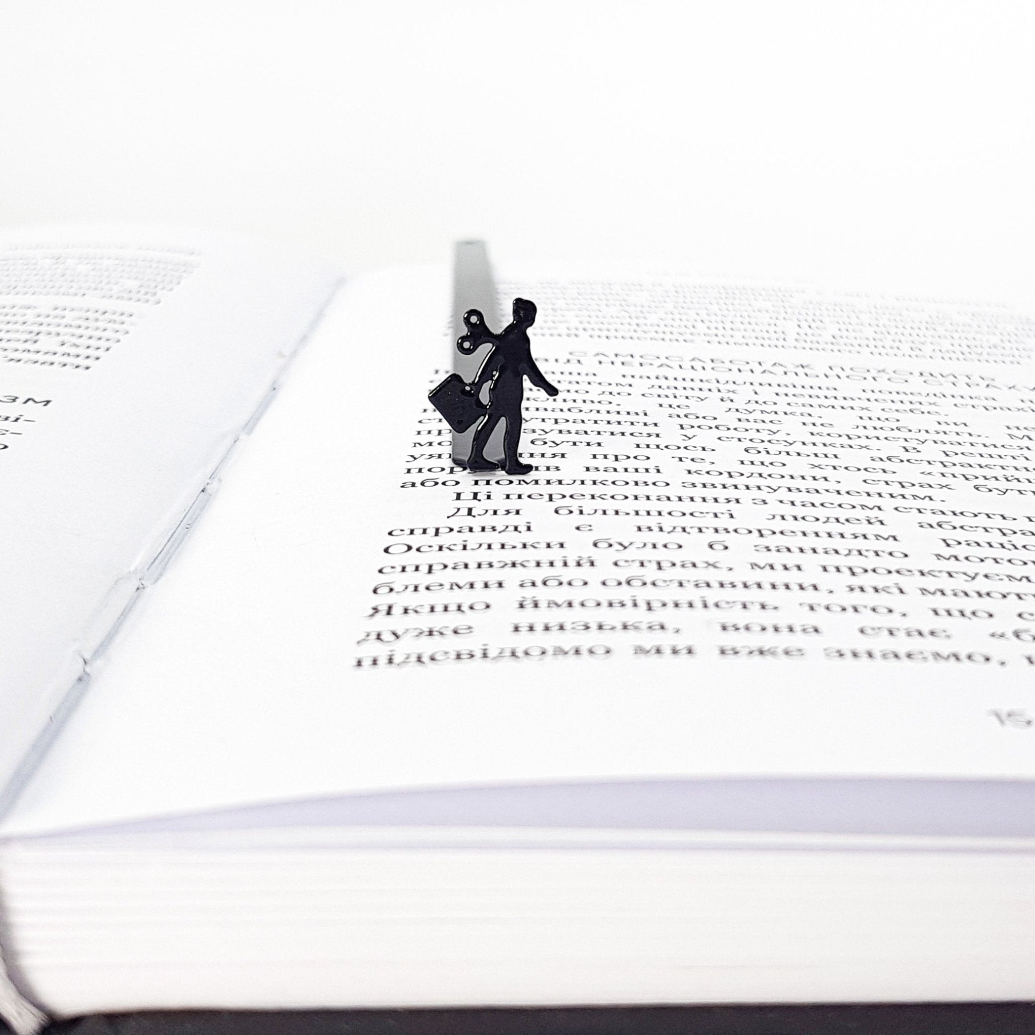 Black metal bookmark with a walking businesswoman silhouette and wind-up key, marking a page inside an open book.