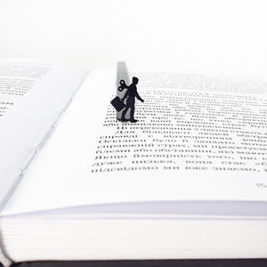 Black metal bookmark with a walking businesswoman silhouette and wind-up key, marking a page inside an open book.
