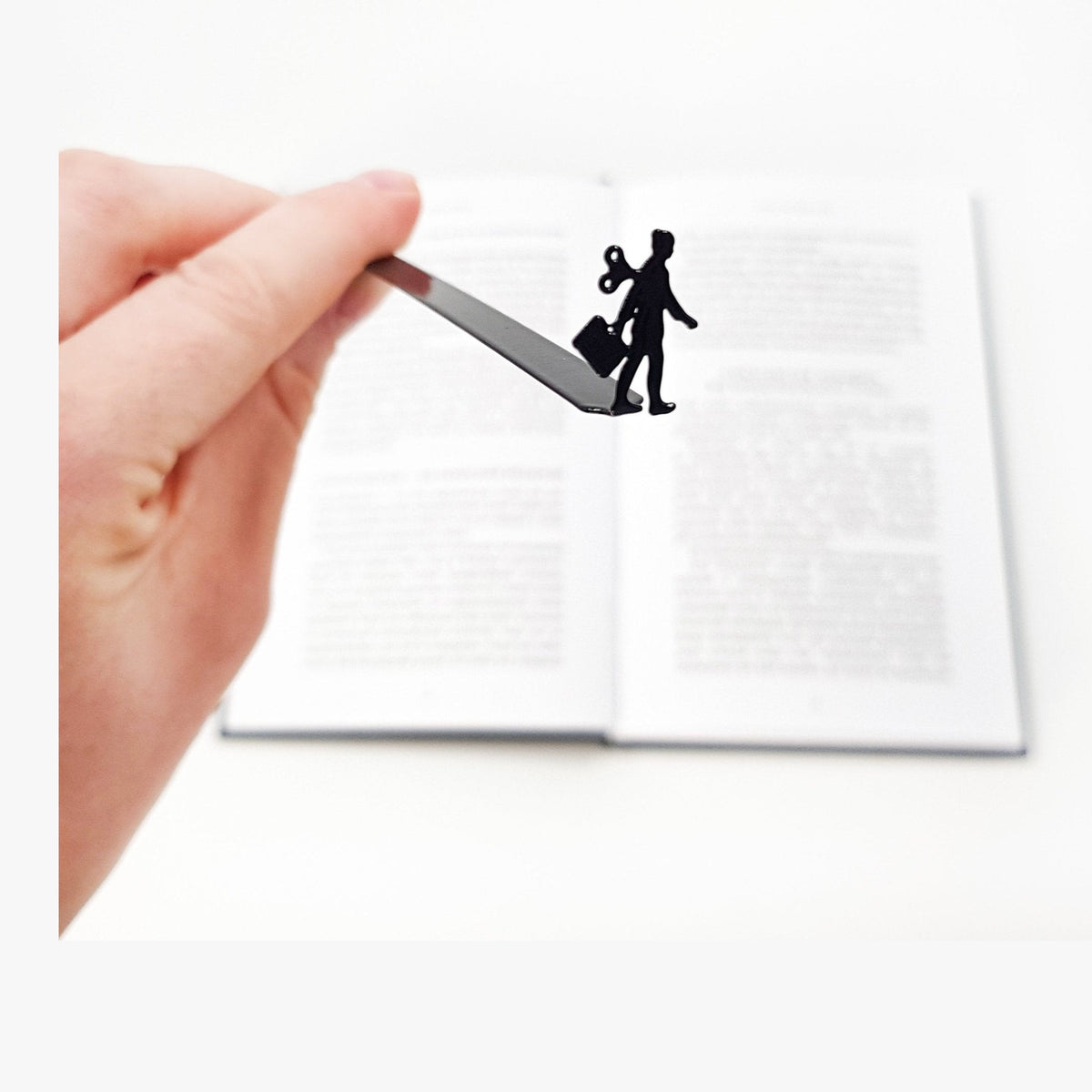 Metal bookmark with Working Woman Silhouette held in a hand above an open book
