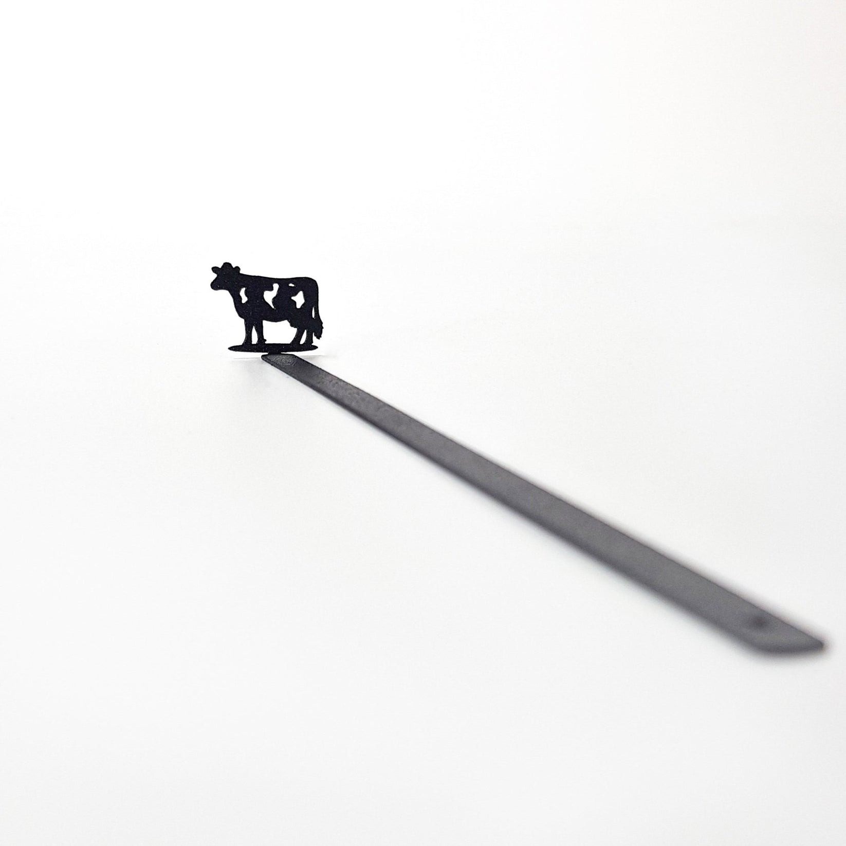 Full product shot — 17 cm laser-cut black steel cow bookmark on white background, diagonal view