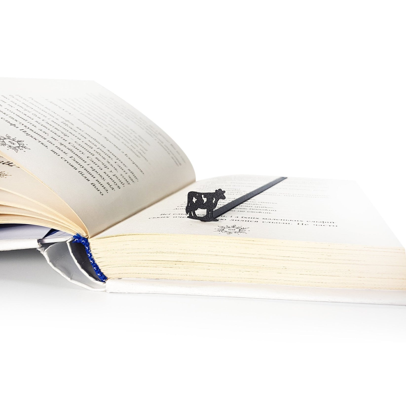 Steel cow bookmark in open book lifestyle shot, warm natural light setting