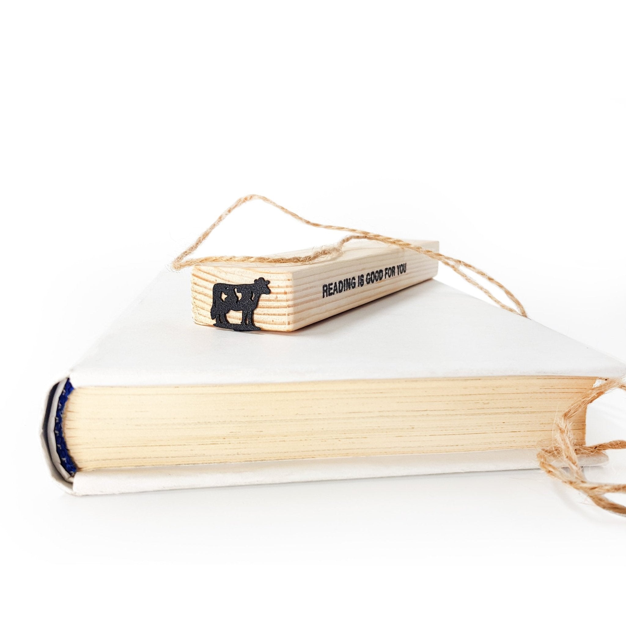 Metal cow bookmark on wooden gift block stamped READING IS GOOD FOR YOU, white background