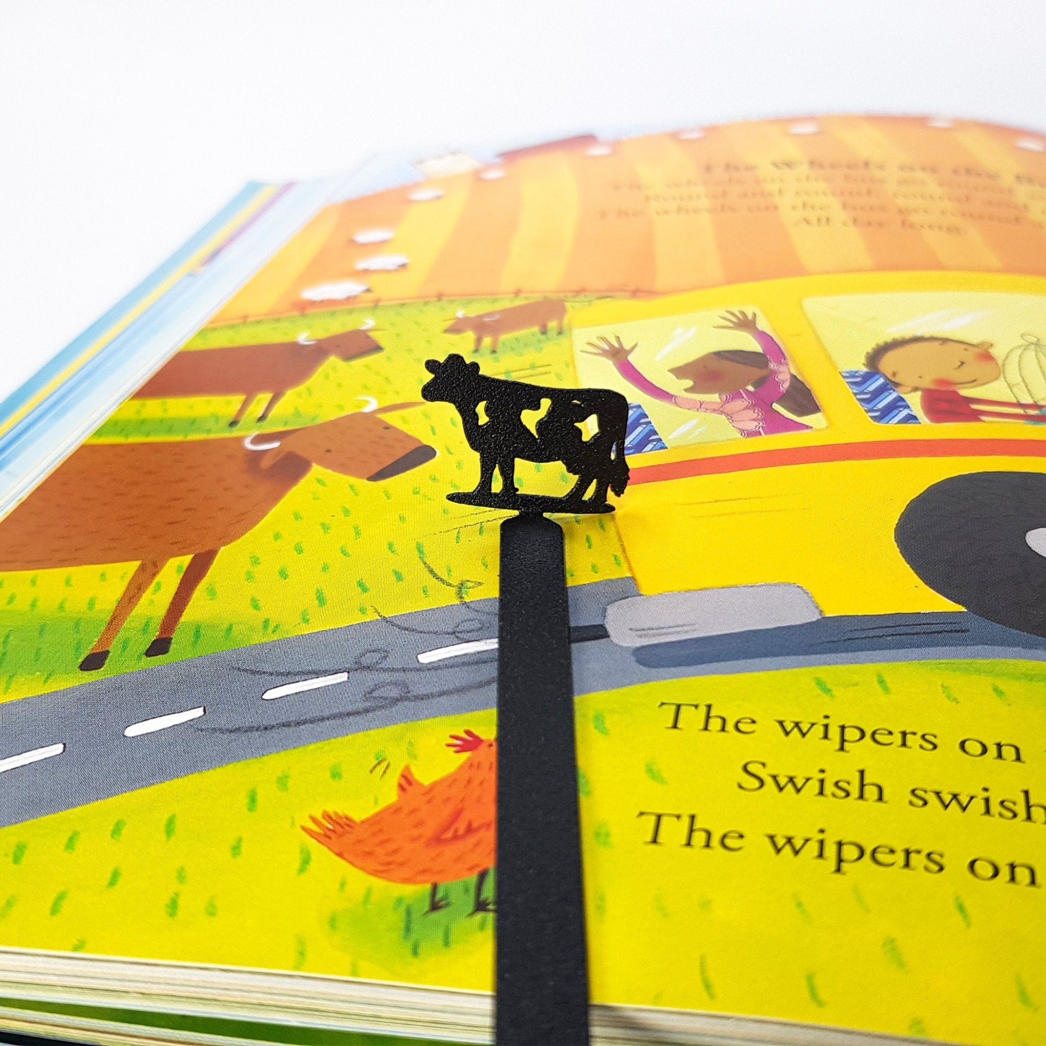 Metal Cow bookmark marking a page in an illustrated book