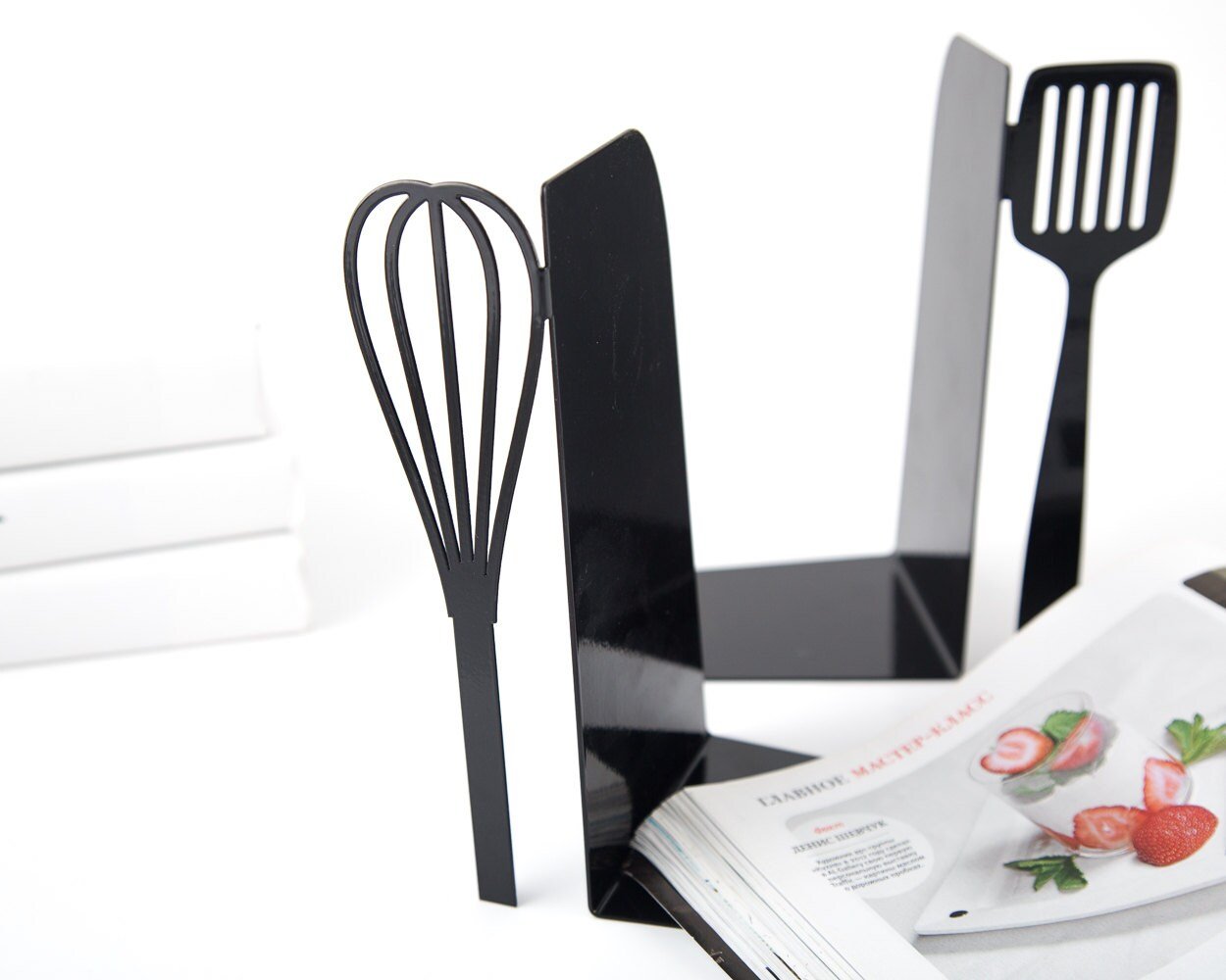 Black spatula and whisk metal bookends holding cookbooks