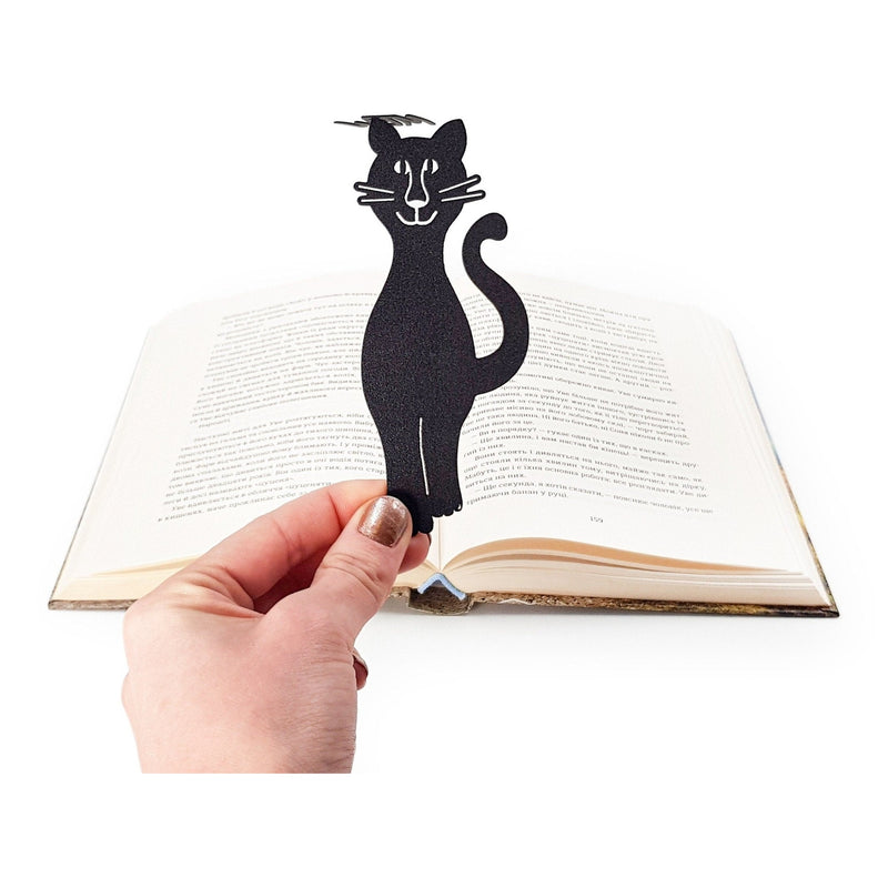 Mew Smiling Cat metal bookmark held in a hand above an open book