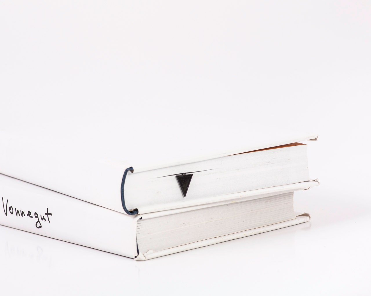 Minimalist Triangle metal bookmark in a closed book, only its top showing above the pages