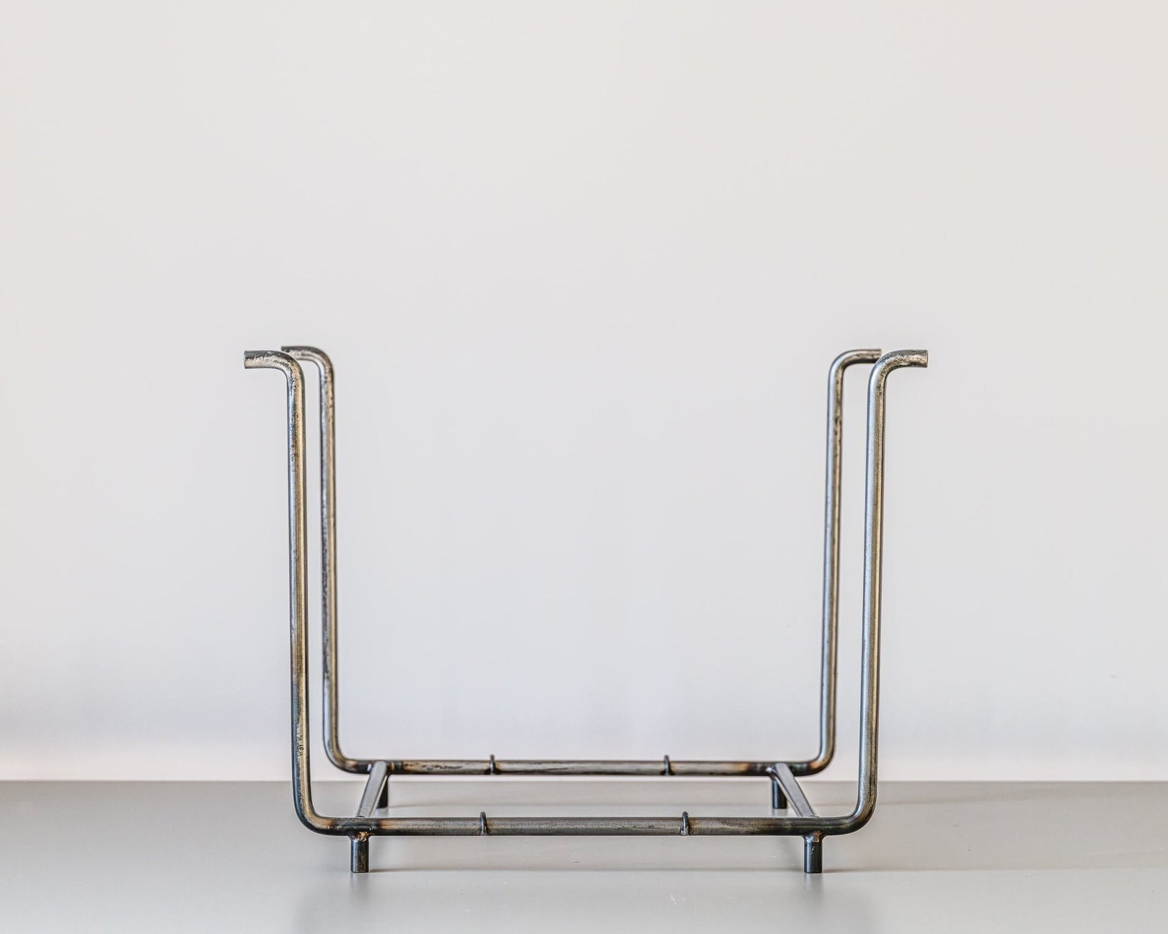 Front view of an empty handcrafted vinyl record rack made of raw steel with tall vertical side frames, placed on a light grey surface against a white background.