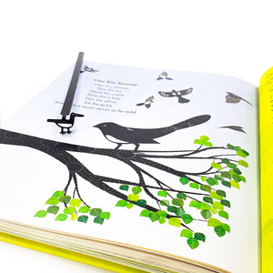 Minimalist black metal bird bookmark marking a page in an illustrated book with bird artwork, showing how the bookmark aligns with the page design.
