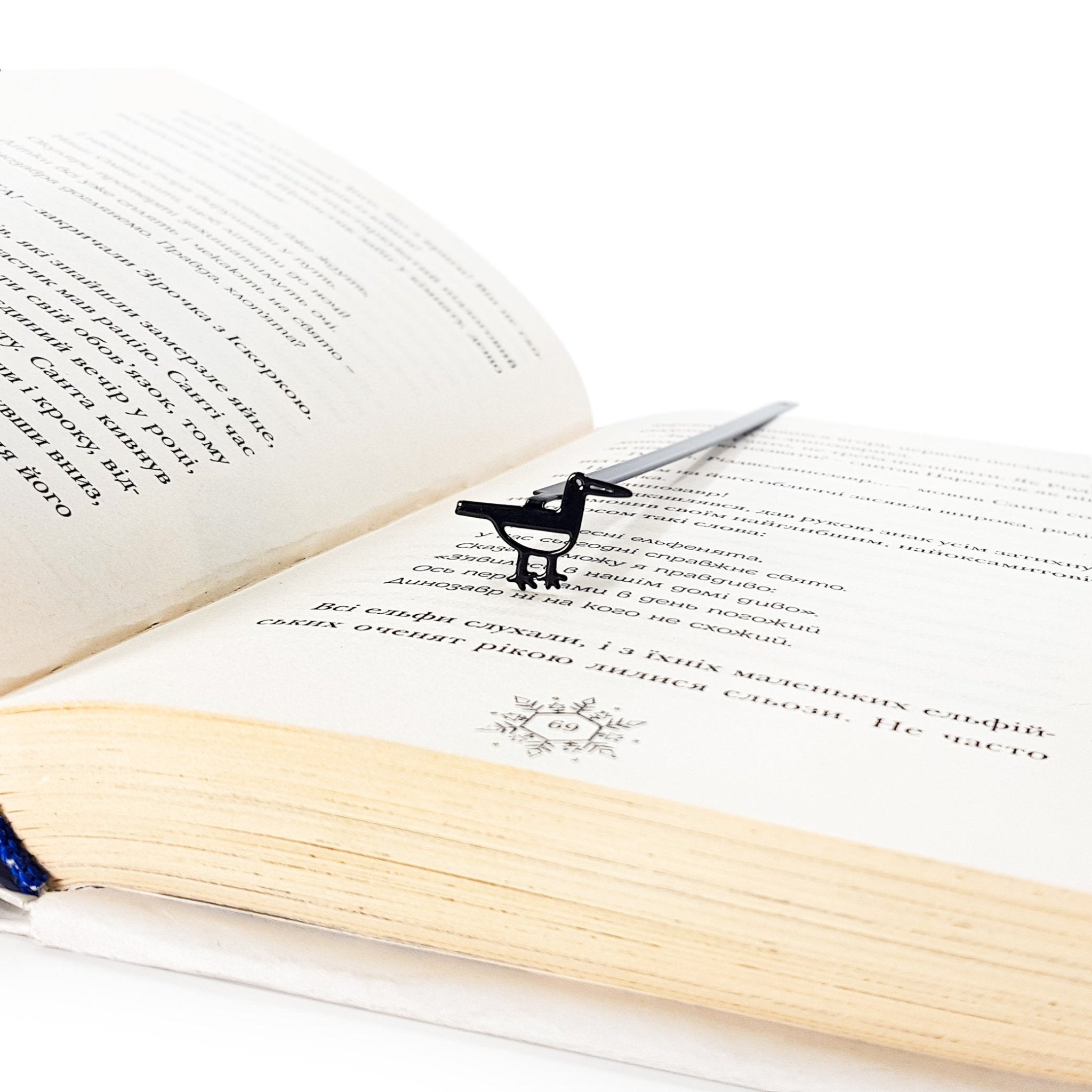 Minimalist black metal bird bookmark resting inside an open book, shown from an angled view to illustrate scale and reading placement.