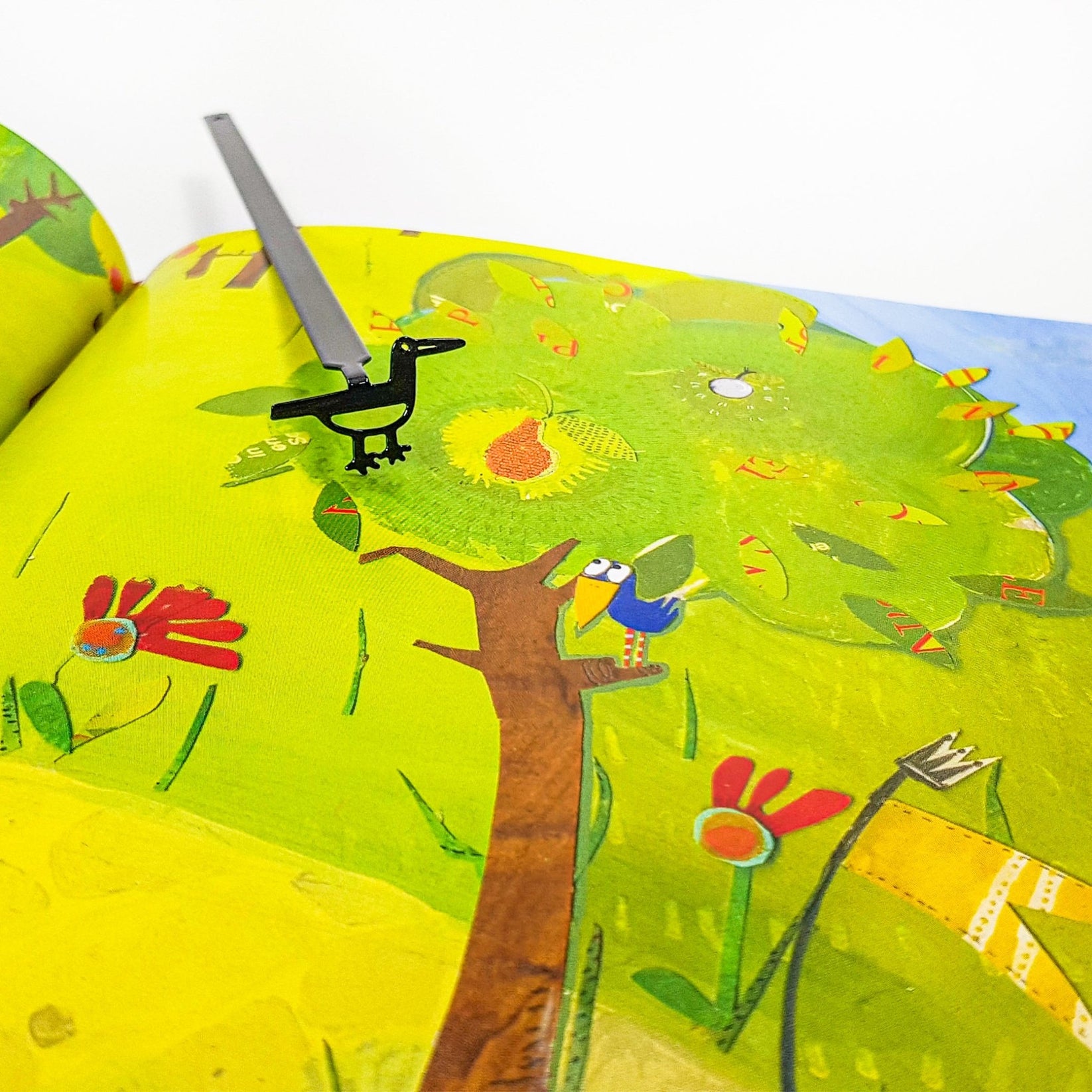 Minimalist black metal bird bookmark placed on a colorful illustrated book page, highlighting the contrast between the simple metal shape and the artwork.
