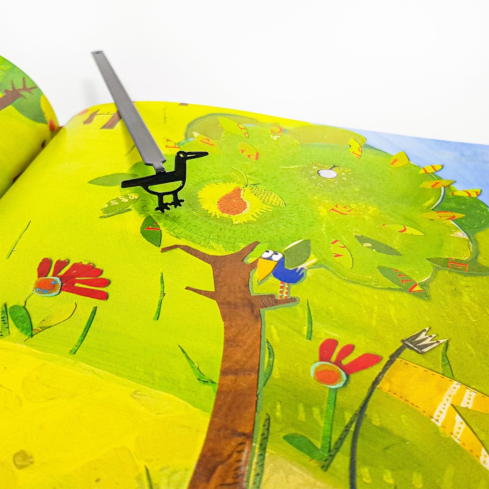 Minimalist black metal bird bookmark placed on a colorful illustrated book page, highlighting the contrast between the simple metal shape and the artwork.