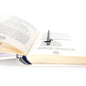 Minimalist black metal bird bookmark positioned in an open book, viewed from an angle to show how it sits between pages while reading.