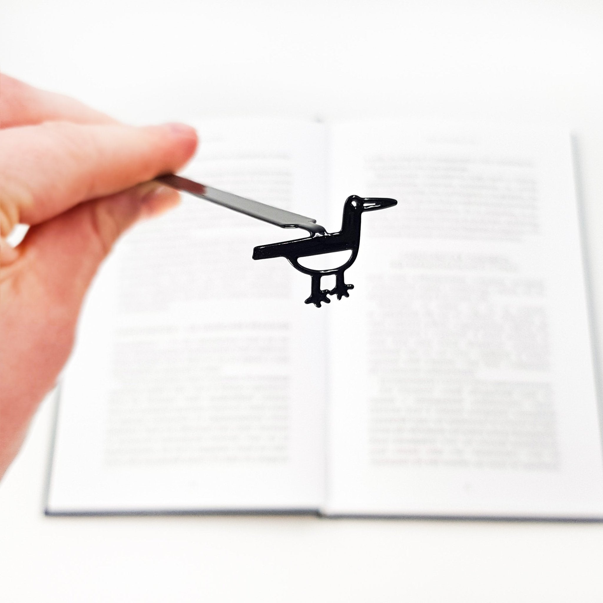 Hand holding a black bird-shaped bookmark over an open book