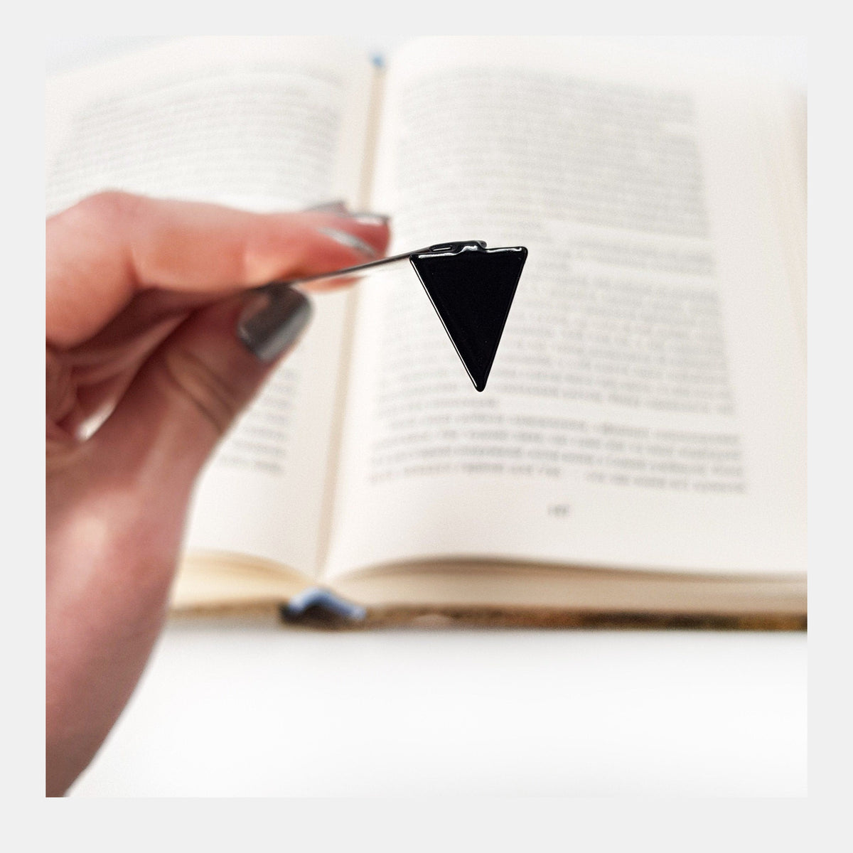 Minimalist Triangle metal bookmark held in a hand above an open book